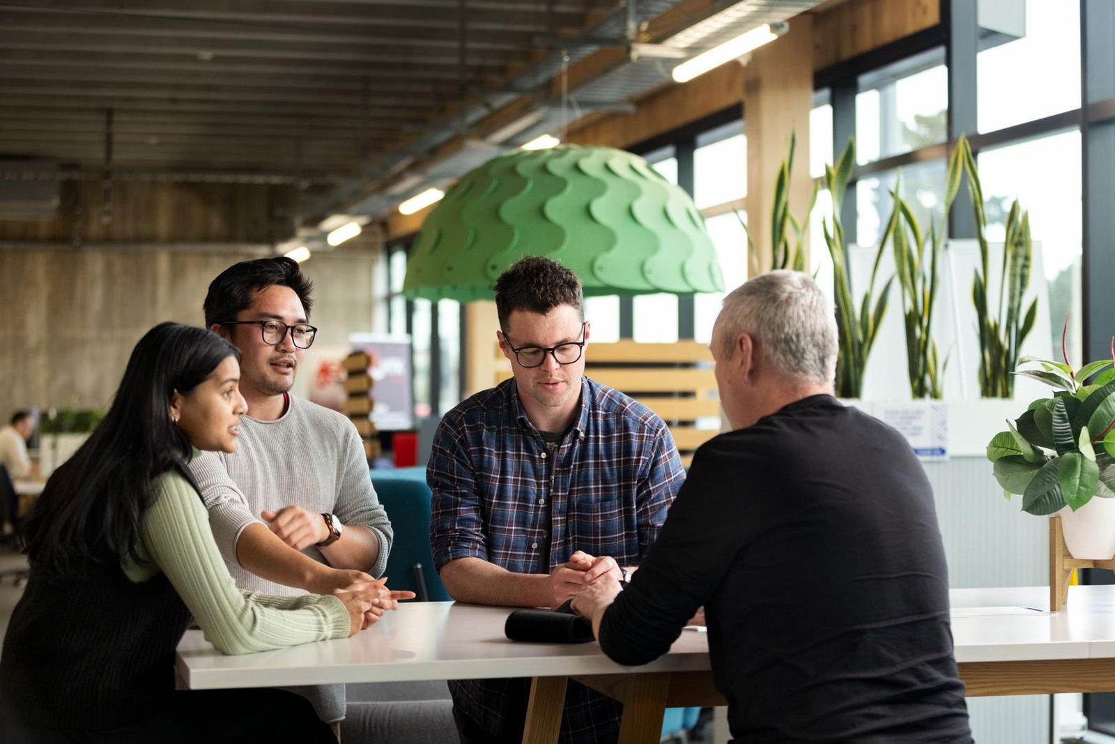 Diverse group of professionals collaborating at a modern table in Christchurch’s Te Ōhaka Innovation Hub.